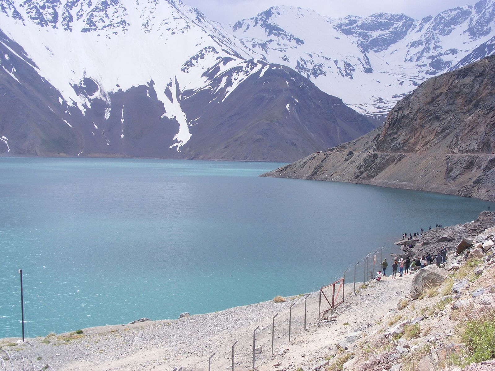 Visitantes olhando o Embalse el Yeso com montanhas nevadas ao fundo